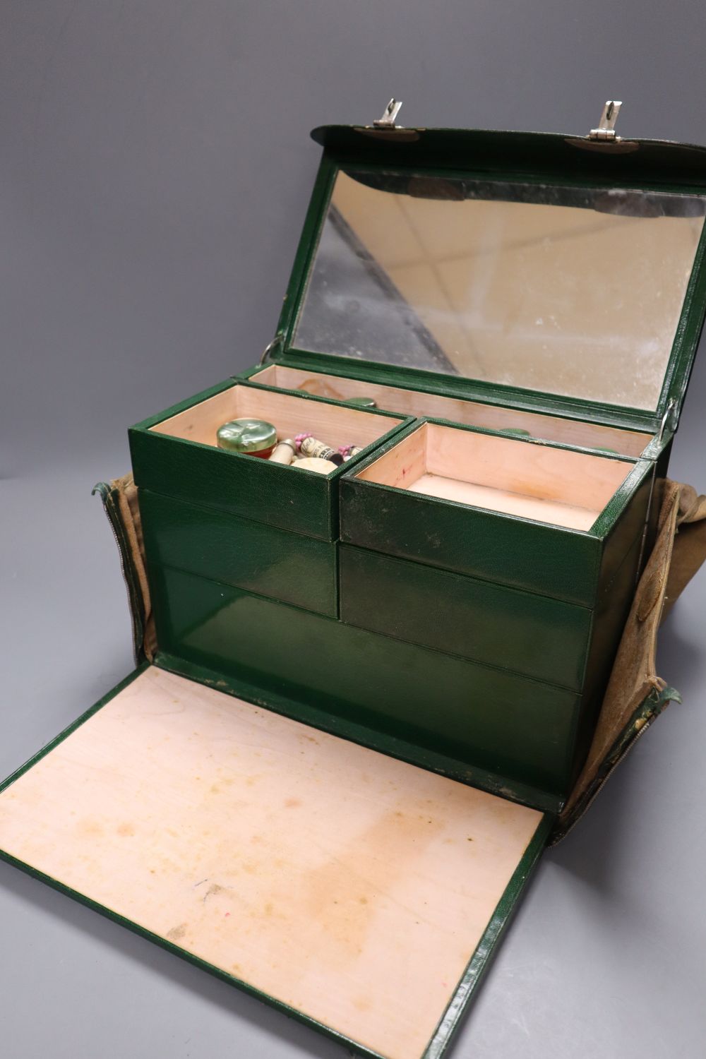 A 1930s ladies green leather travelling toilet case, fittings include seven glass and enamelled bottles, 32cm, in original travelling